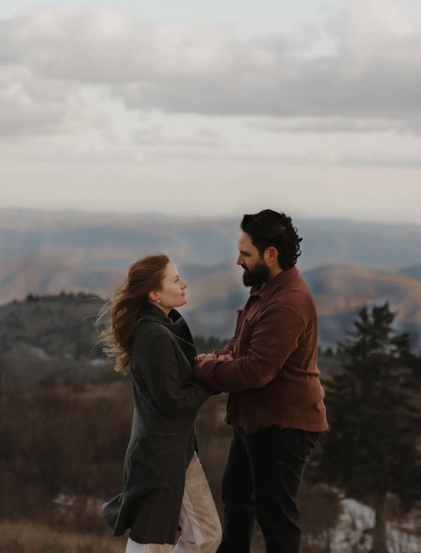 Engaged couple sharing a quiet moment on a mountain overlook with blue ridges behind them