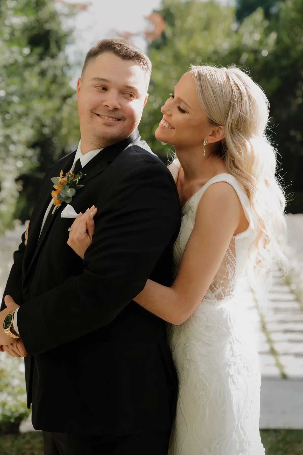Bride hugging her groom from behind as he smiles outside the venue